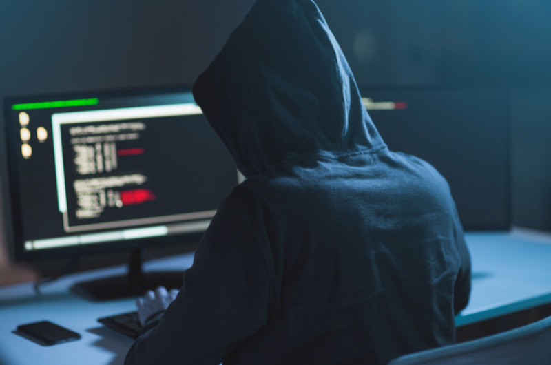 hooded hacker typing code on computer